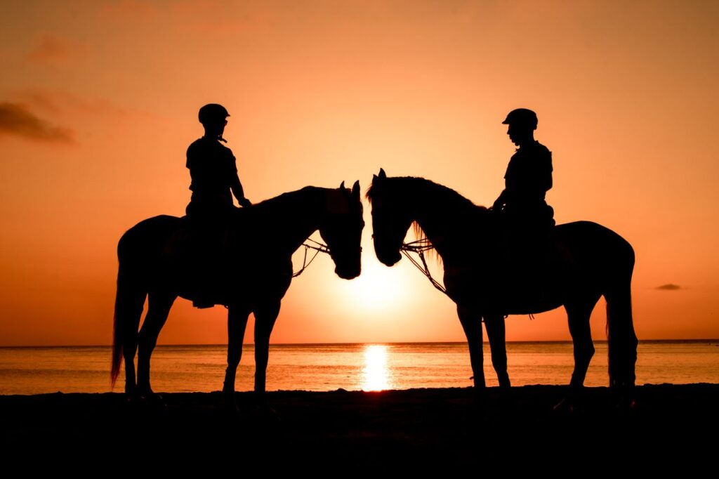 Two horseback riders silhouetted against a vibrant sunset on the beach.
